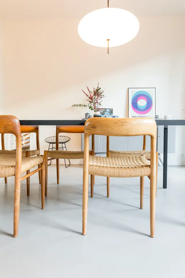 Minimalistisch ingerichte eetkamer met houten stoelen en tafel op een perfecte, lichte naadloze vloer. Rustige sfeer met natuurlijk licht, groene planten en discrete wanddecoratie.