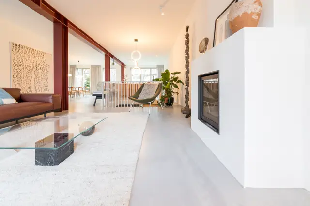 Ruime, licht ingevallen woonkamer met naadloze lichte vloer die naadloos overgaat in aangesloten ruimtes. Minimalistisch inericht met warme accenten en strakke lijnen.