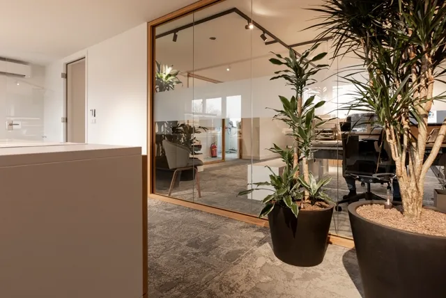 Strak ingerichte bedrijfsruimte met naadloze vloer in warm grijs en grote glazen wanden. Natuurlijk licht, duurzaam ingericht met planten en minimalistisch design.