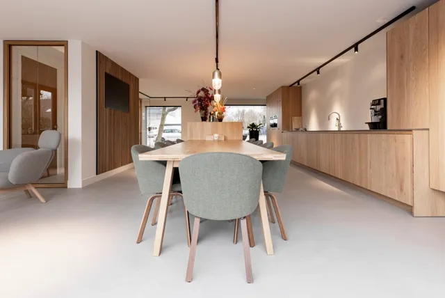 Ruime, heldere woonkeuken met houten meubels en natuurlijk licht. De naadloze vloer zorgt voor een serene, gestroomlijnde uitstraling in warme beige tonen.